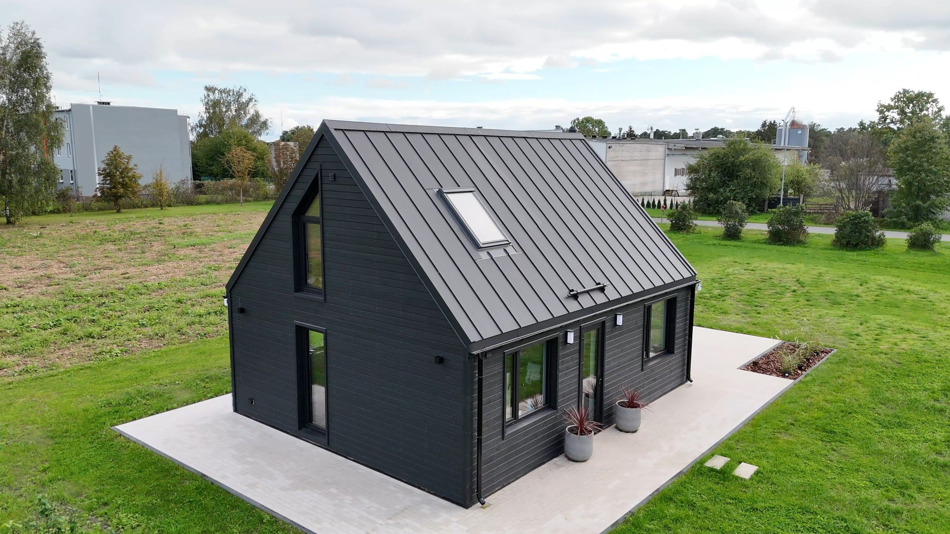 Modern black wooden house with a steep metal roof and skylight, surrounded by a green lawn.