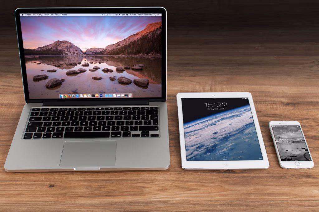 Silver laptop, white tablet, and white smartphone are shown on a wooden surface.