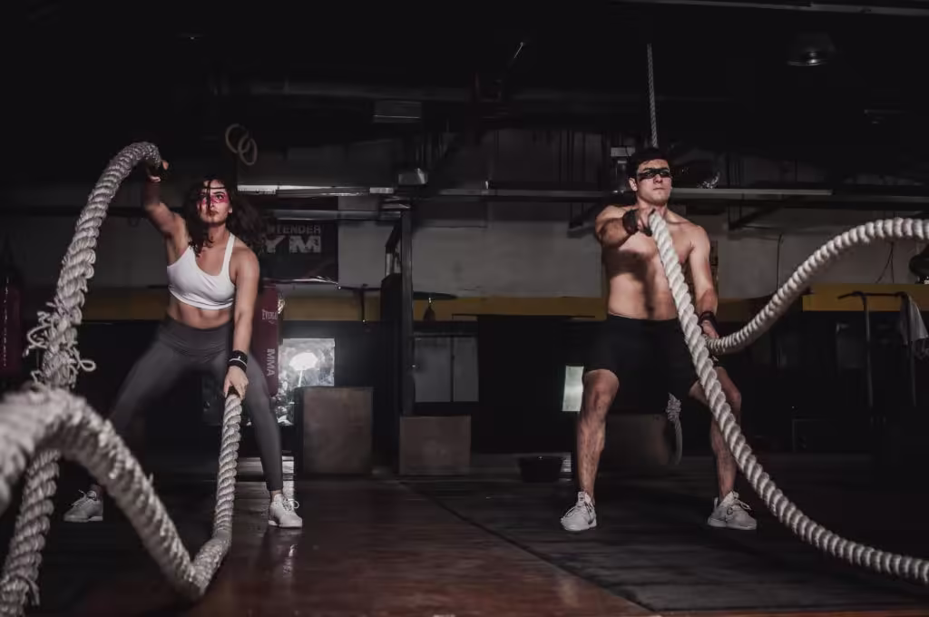 People in a gym doing battle ropes, wearing athletic gear and face paint and in motion.
