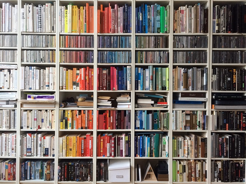 White bookshelves display books and CDs, arranged by color, creating a rainbow effect.
