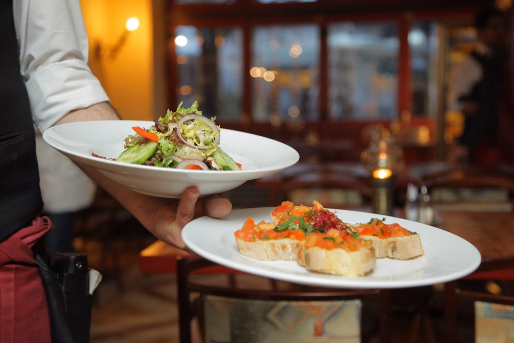 Waiter carrying plates with a salad and bruschetta in a restaurant.