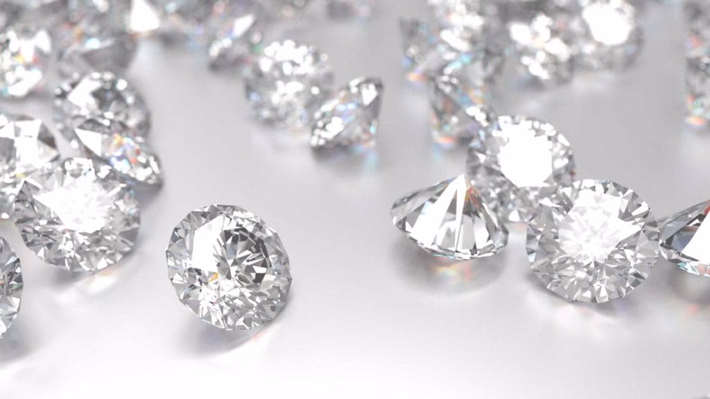Scattered, clear diamonds sparkle as they lie on a reflective surface.