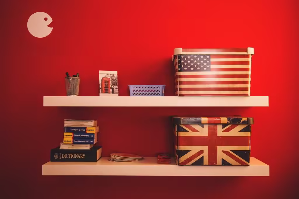 Two shelves hold a Union Jack box, an American flag box, books, and decorations on a red wall.
