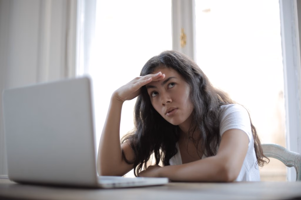 Frustrated woman with head in hand looks away from her laptop.