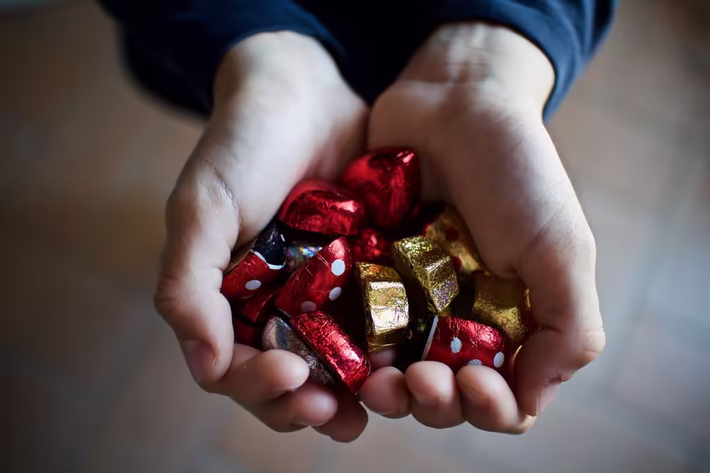 Person holds a handful of gold-wrapped and red-wrapped chocolates.