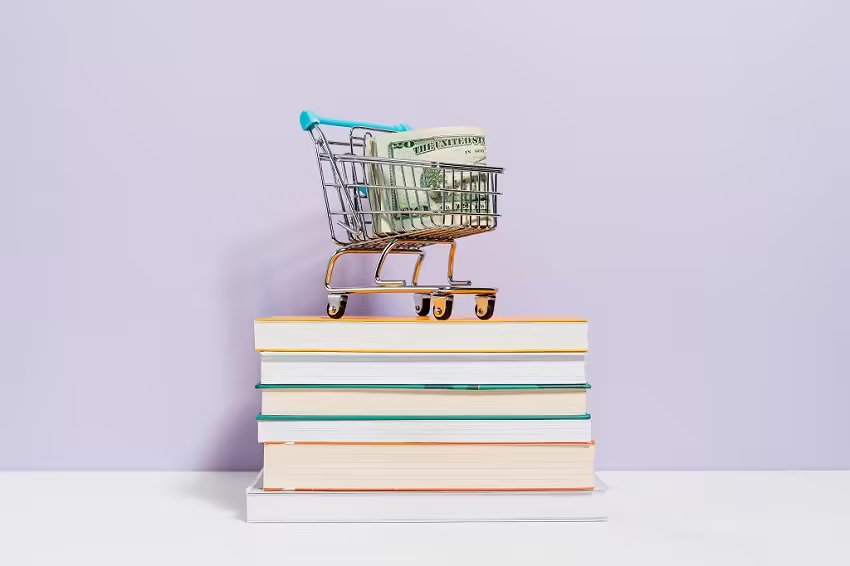 Toy shopping cart with cash sits on a stack of books.
