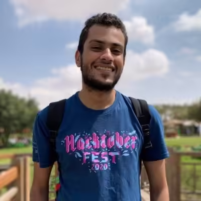 Smiling man wearing a Hacktoberfest 2020 tee shirt and backpack outside.