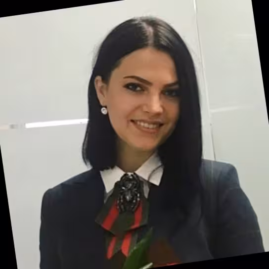 Woman in dark suit, white shirt, and bow with bug brooch smiles; she has short, dark hair.