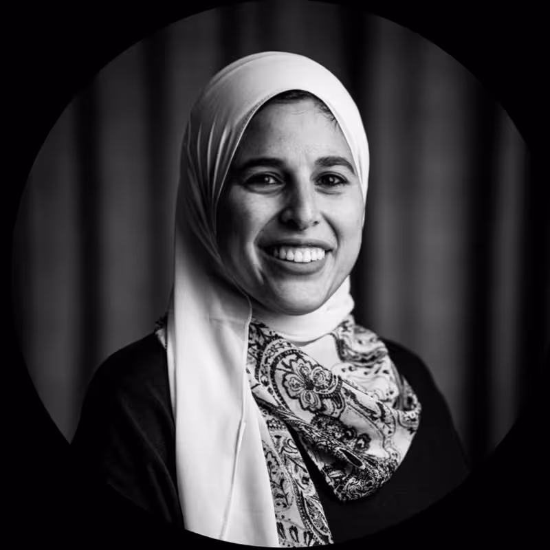 Black and white portrait of a smiling woman wearing a hijab and patterned scarf.