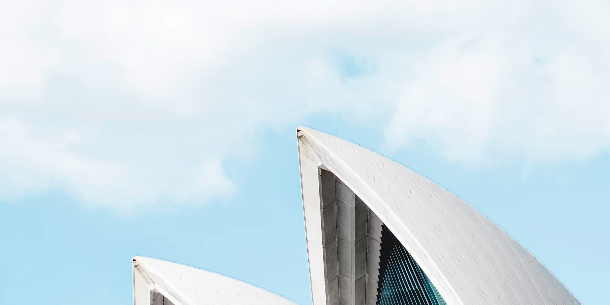 Vue en gros plan des voiles blanches du bâtiment emblématique de l'Opéra de Sydney sur fond de ciel bleu clair avec des nuages.
