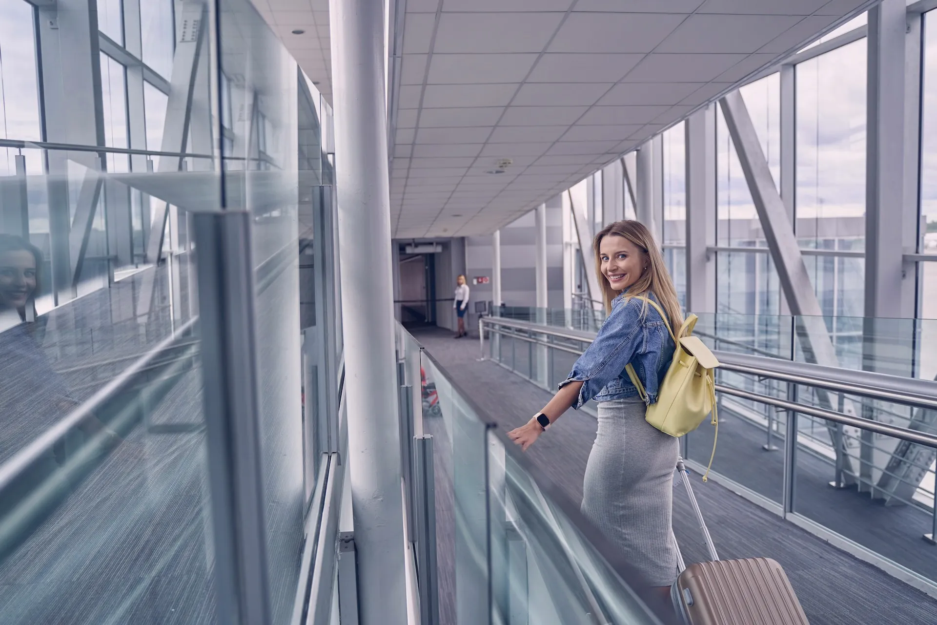 Photo d'une voyageuse souriante, tirant sa valise dans le couloir d'un aéroport.
