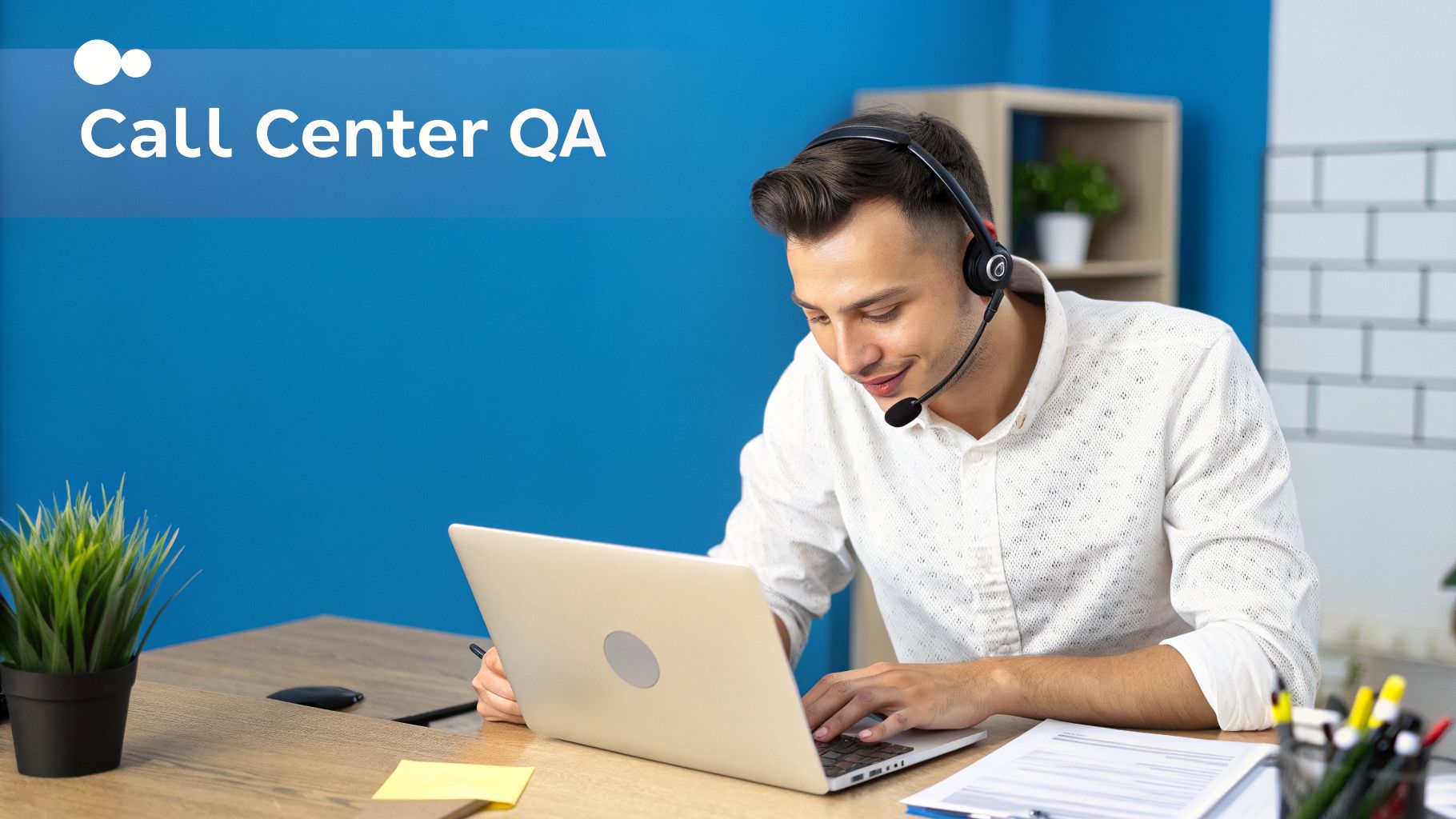 A smiling call center agent wearing a headset, typing on a laptop at his desk.