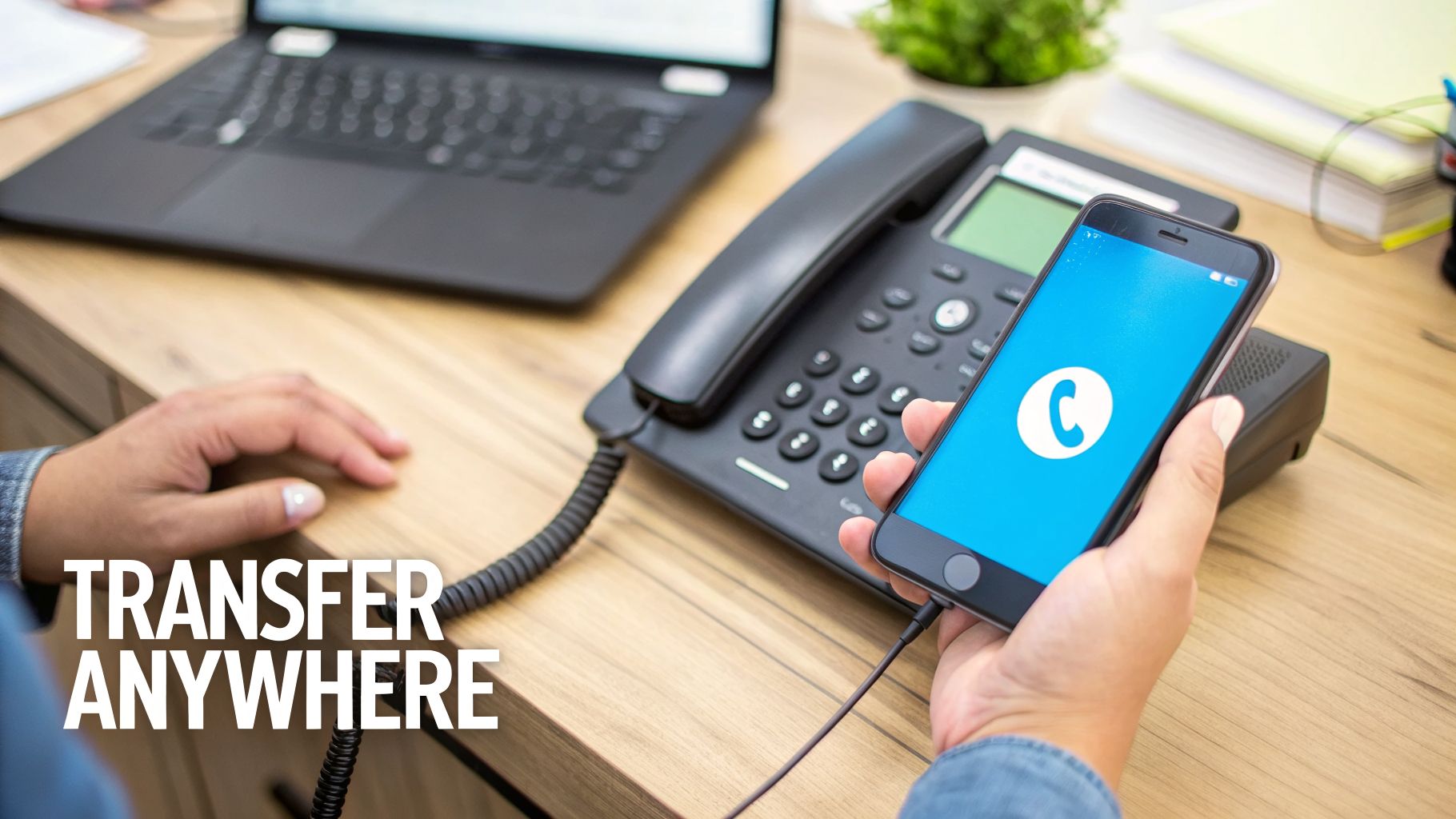 A person holds a smartphone with a blue app screen next to a desk phone and laptop.