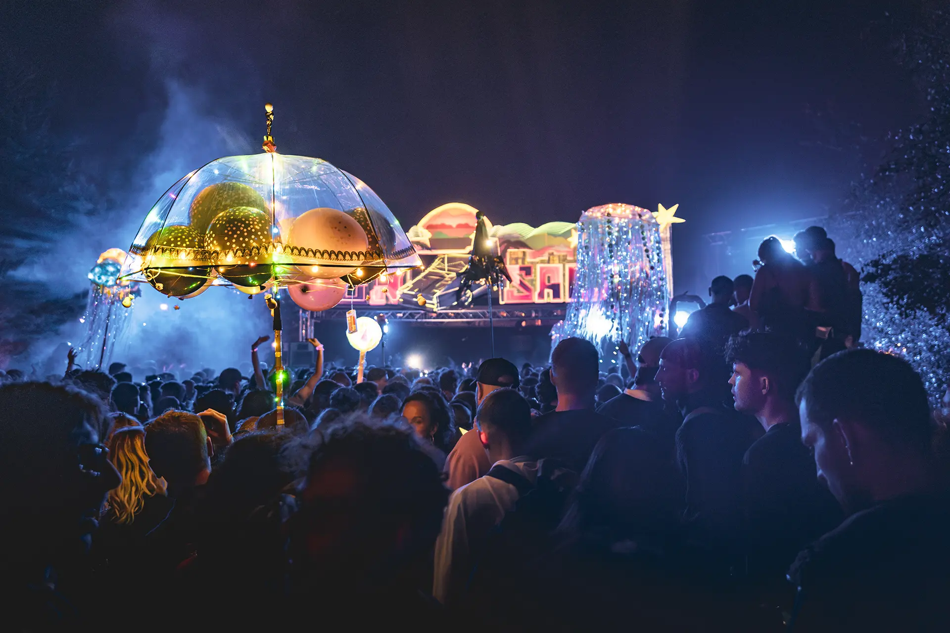 Menschen vor einer Bühne, es sind mehrere Leuchtstäbe in der Luft zu sehen.