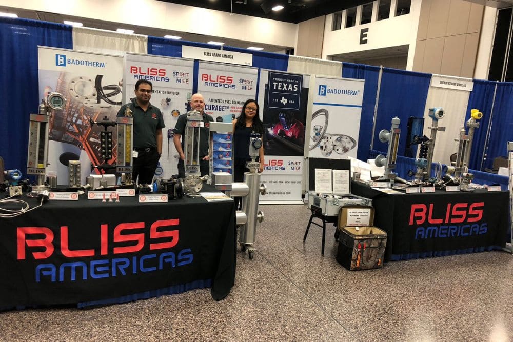 Bliss Americas booth at trade show with industrial measurement instruments and three representatives.