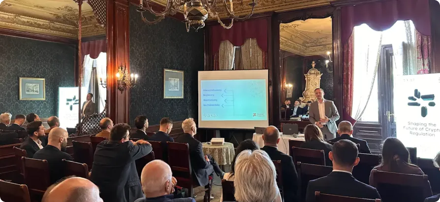 Man giving a presentation on crypto regulation in a formal room filled with attentive audience members.