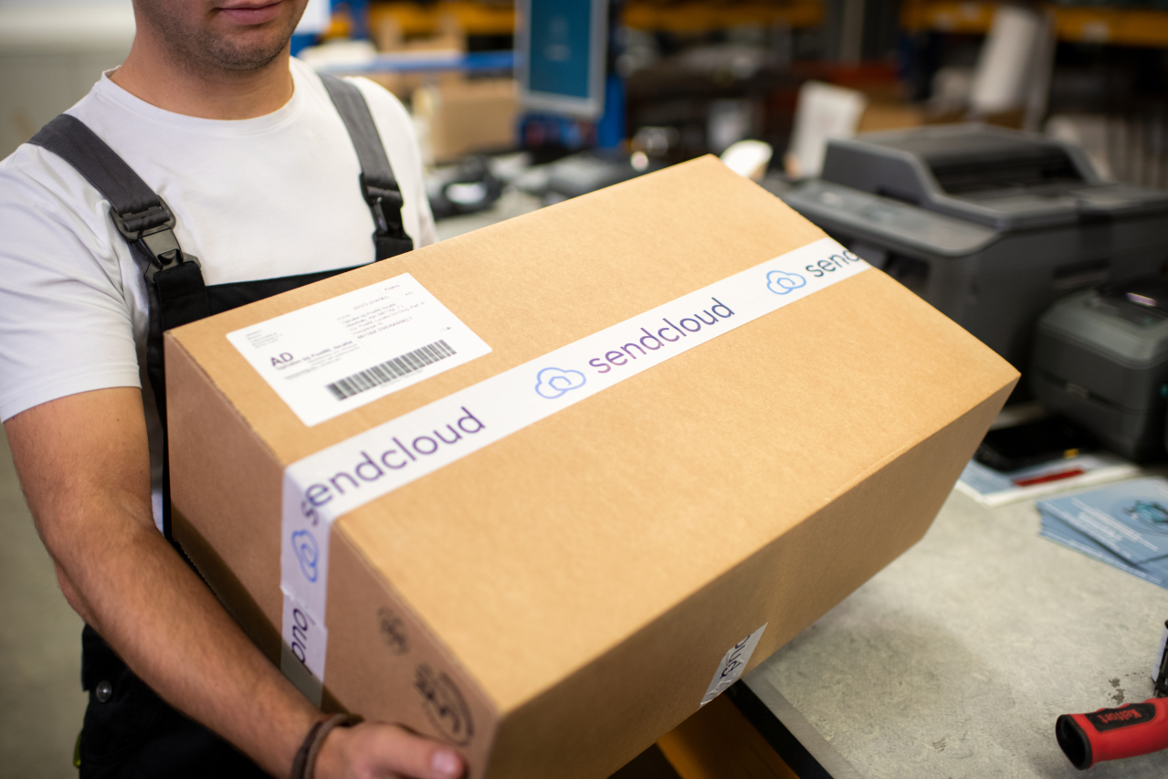 Mitarbeiter:in verpackt eine Bestellung am Packtisch – der Moment, in dem die Versandkommunikation startet.