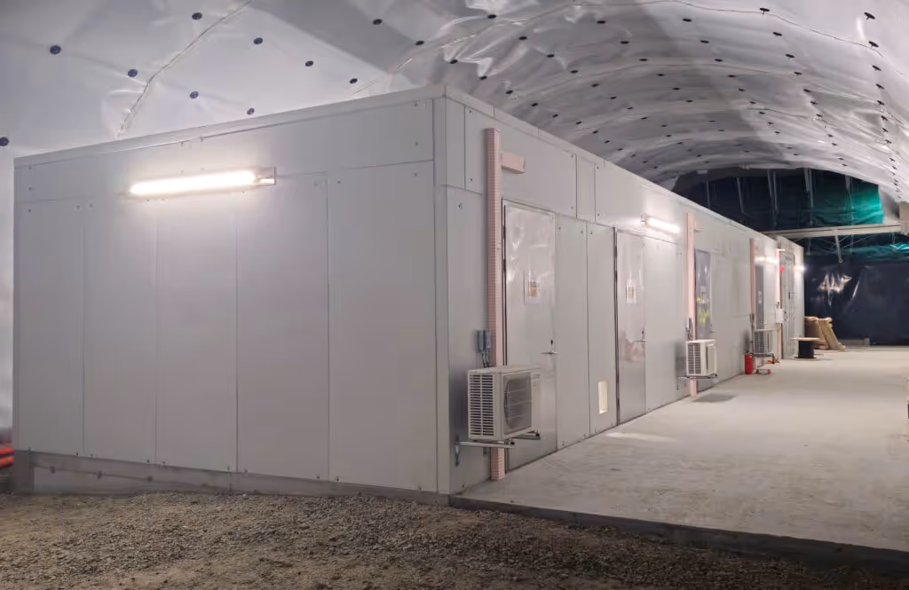 Langt midlertidig modulbygg med flere dører og veggmonterte klimaanlegg under en oppblåsbar takstruktur.