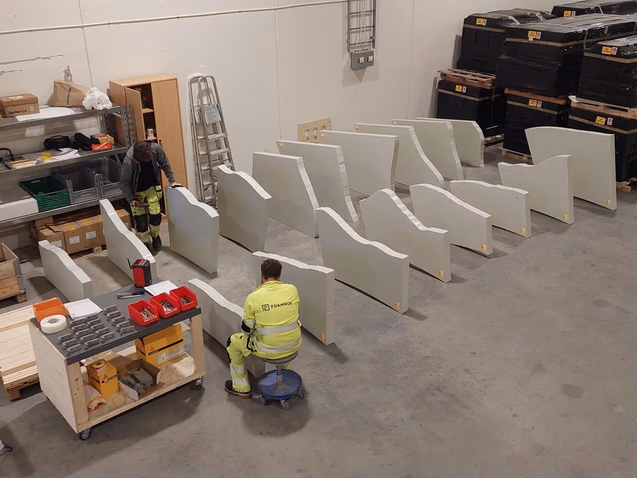 To arbeidere i en verkstedhall med flere store, hvite støpte former arrangert i rader på gulvet.