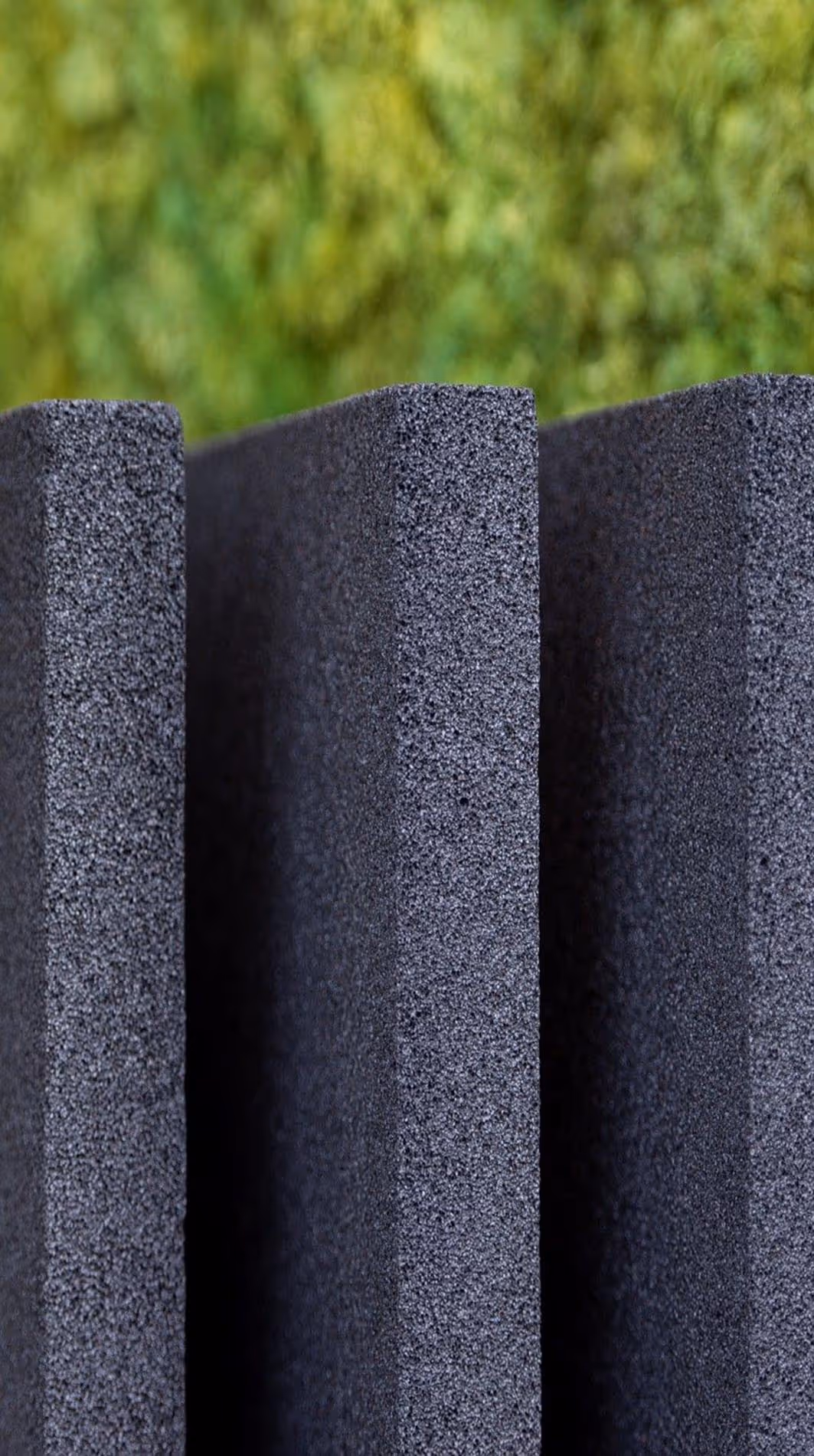 Nærbilde av stående svarte skumplater med grov tekstur, mot en uskarp grønn bakgrunn.