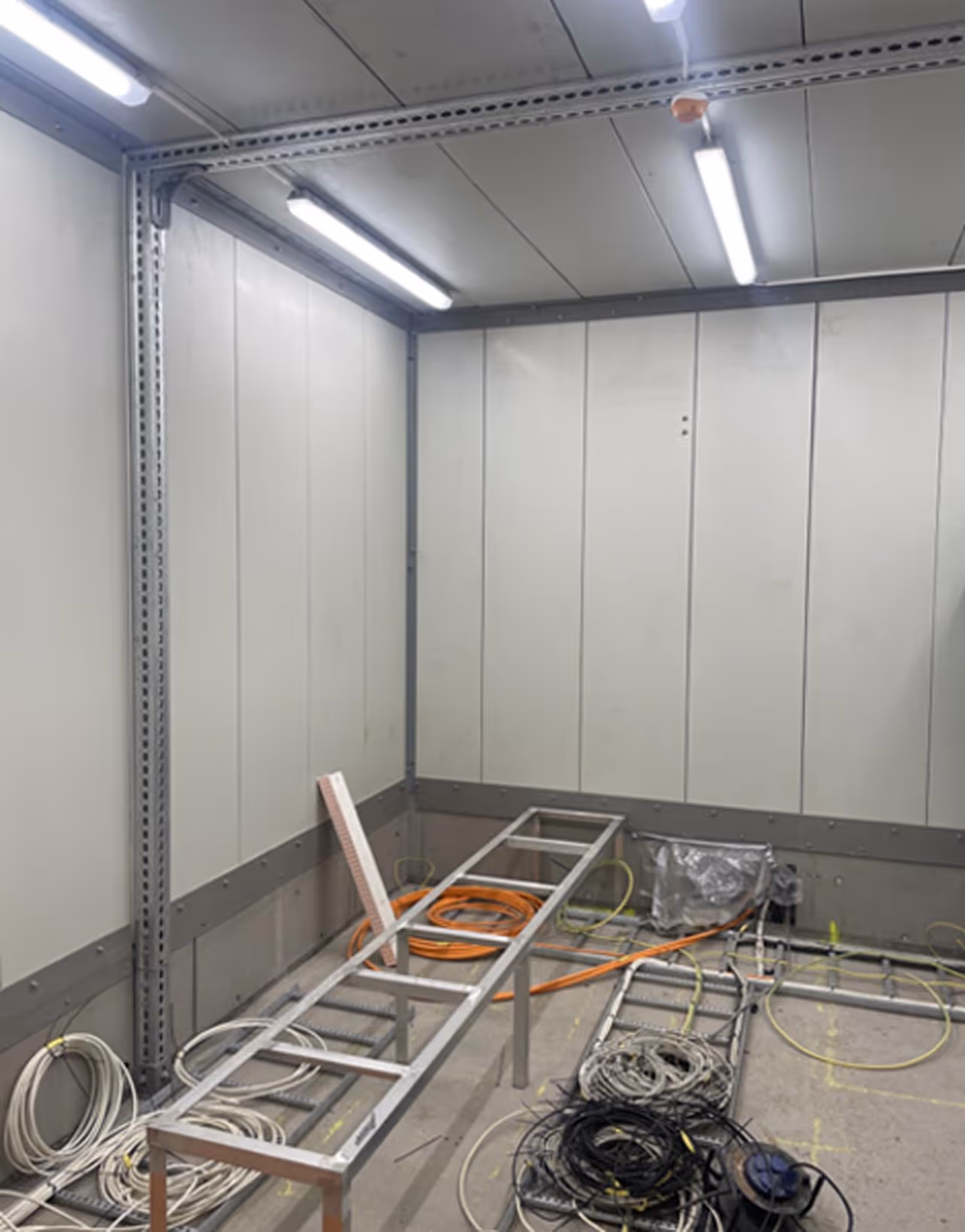 Innvendig hjørne av et teknisk rom med kabelstiger og sammenrullede elektriske kabler på gulvet.