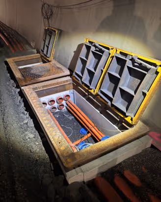 Åpen kabelgrøft med trekkerør og fordelerbokser på et bygge- eller anleggsområde om natten.