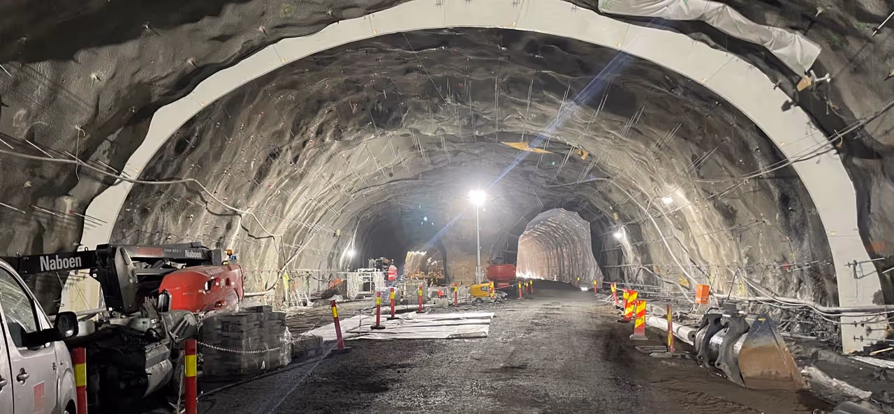 Underjordisk tunnel under konstruksjon med maskiner, materialer og midlertidig belysning.