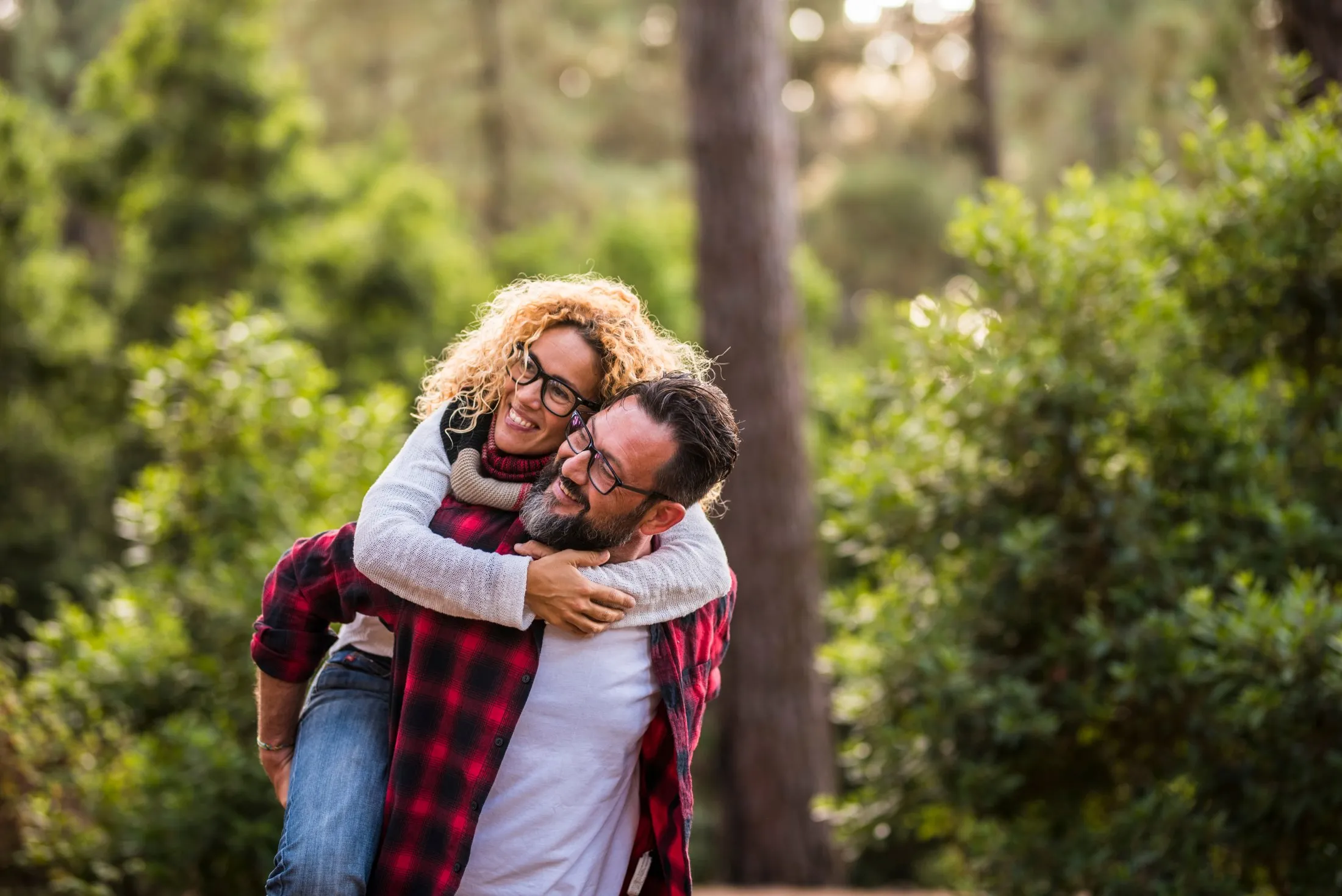 Couple hugging and smiling in lush forest with sunlight filtering through trees