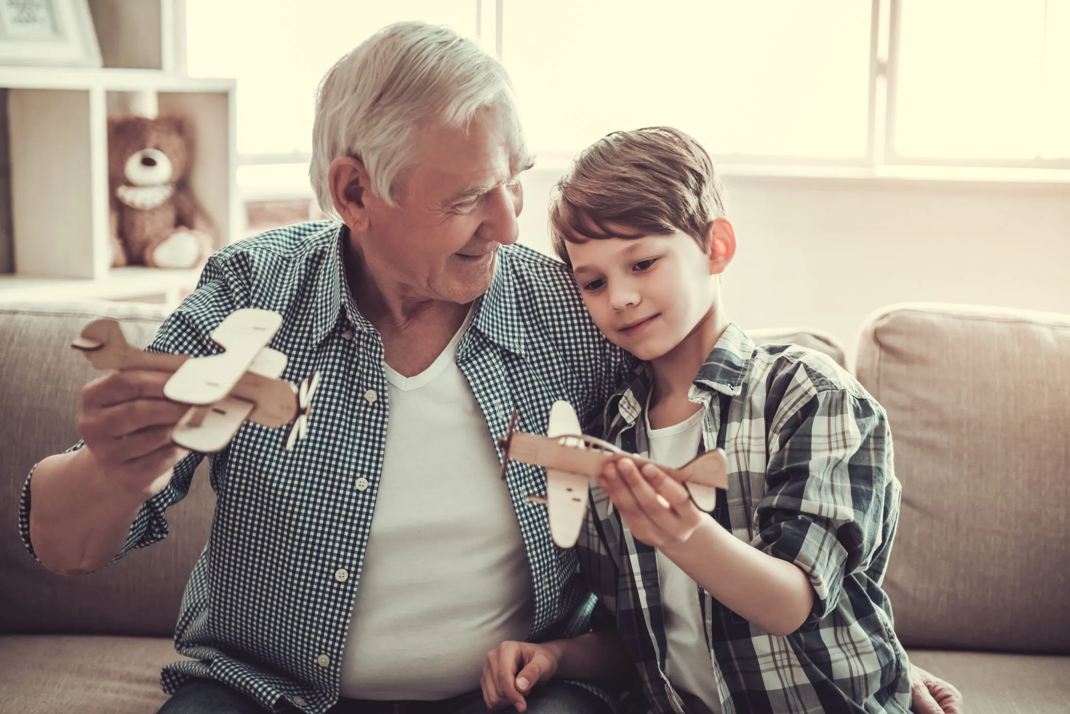 Grandfather and grandson playing with wooden airplane together on sofa