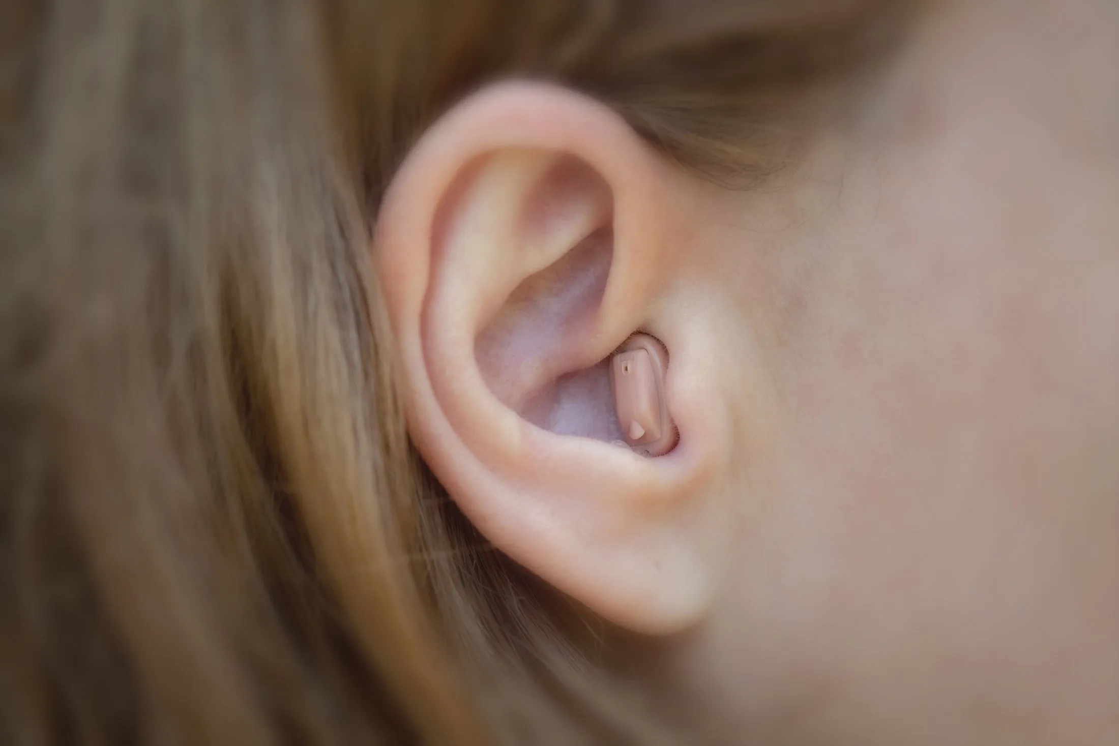 Wireless earbud inserted in ear with blurred hair and skin background