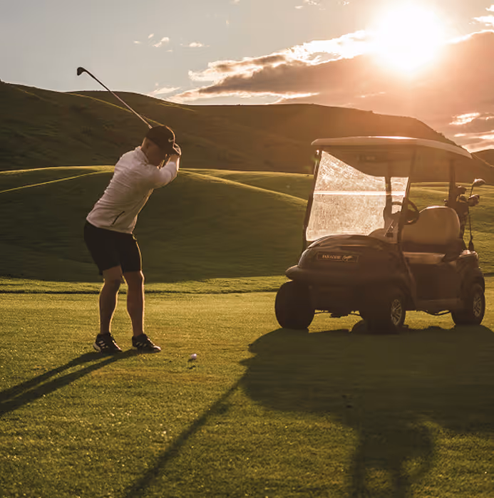 A man plays golf on a course next to a golf cart.