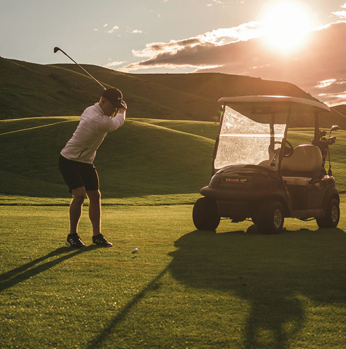 A man plays golf on a course next to a golf cart.