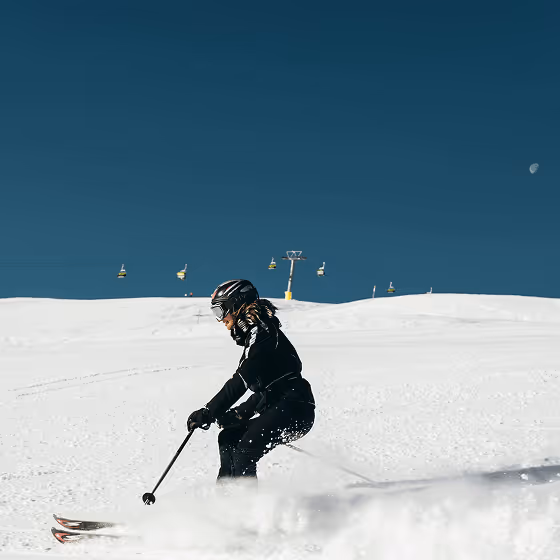 A skier skis against the backdrop of snow and a cable car.