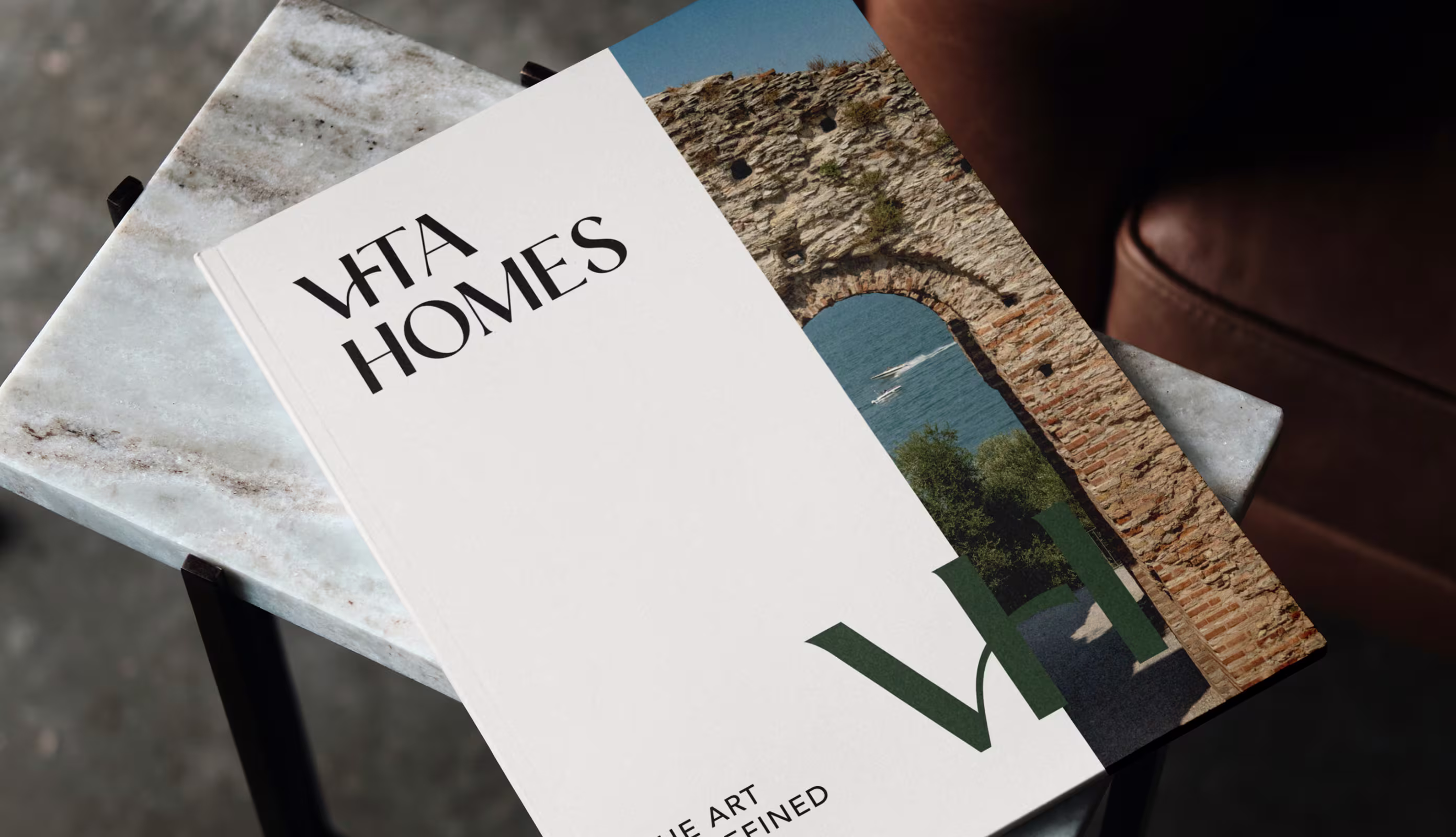White book titled 'VFTA HOMES' with stone arch and water photo on cover lying on marble table.