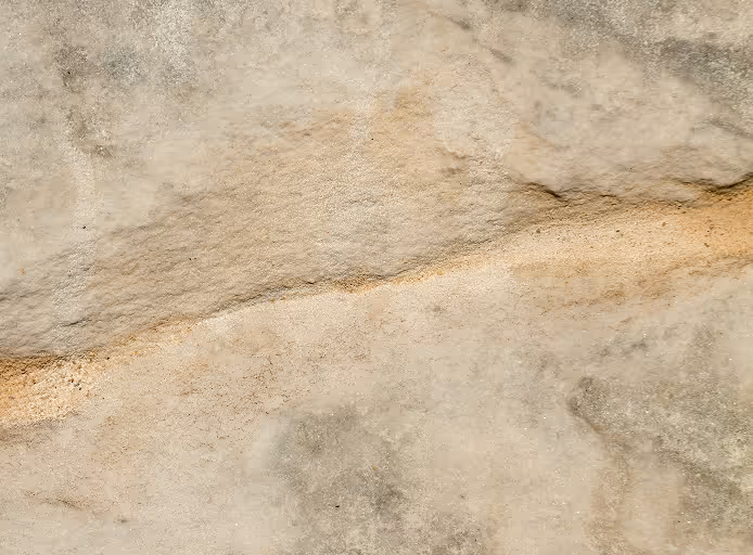 Close-up of a textured beige and gray stone surface with natural cracks and patterns.