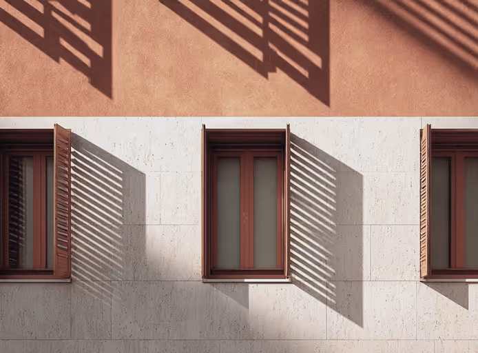 Three wooden windows on a beige wall casting long striped shadows from their shutters.