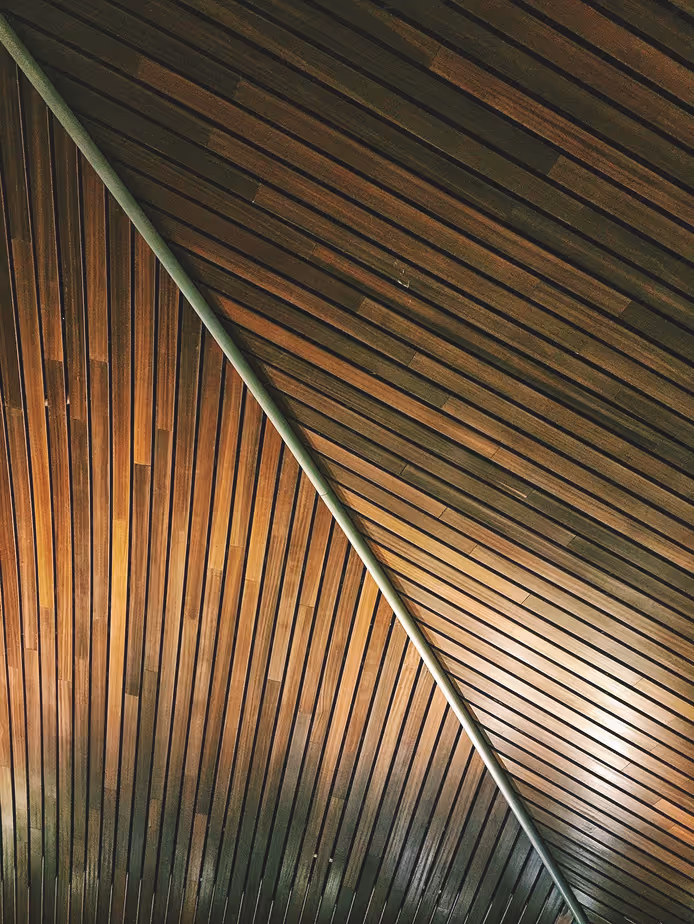 Wooden ceiling panels arranged diagonally with a metal divider creating contrasting angles.