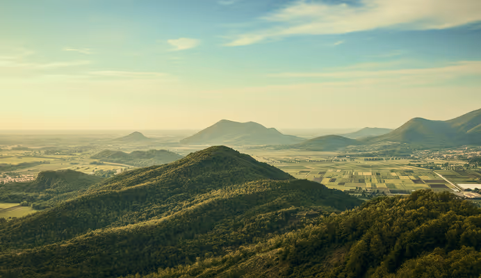 Green forested hills with farmland and mountains under a partly cloudy blue sky.