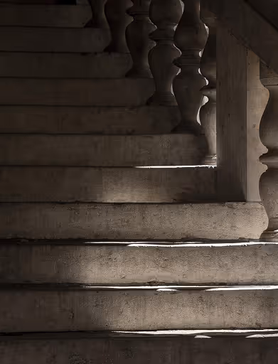 Stone staircase with ornate balusters, lit by soft natural light creating shadows on steps.