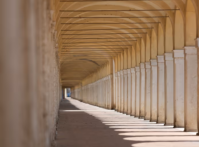 Long corridor with repeating arches and columns casting shadows under warm light.