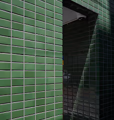 Dark green tiled walls forming a corner with a shadowed opening creating a diagonal light pattern.