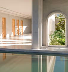 Indoor pool with large windows showing greenery and wooden doors with sunlight streaming in.