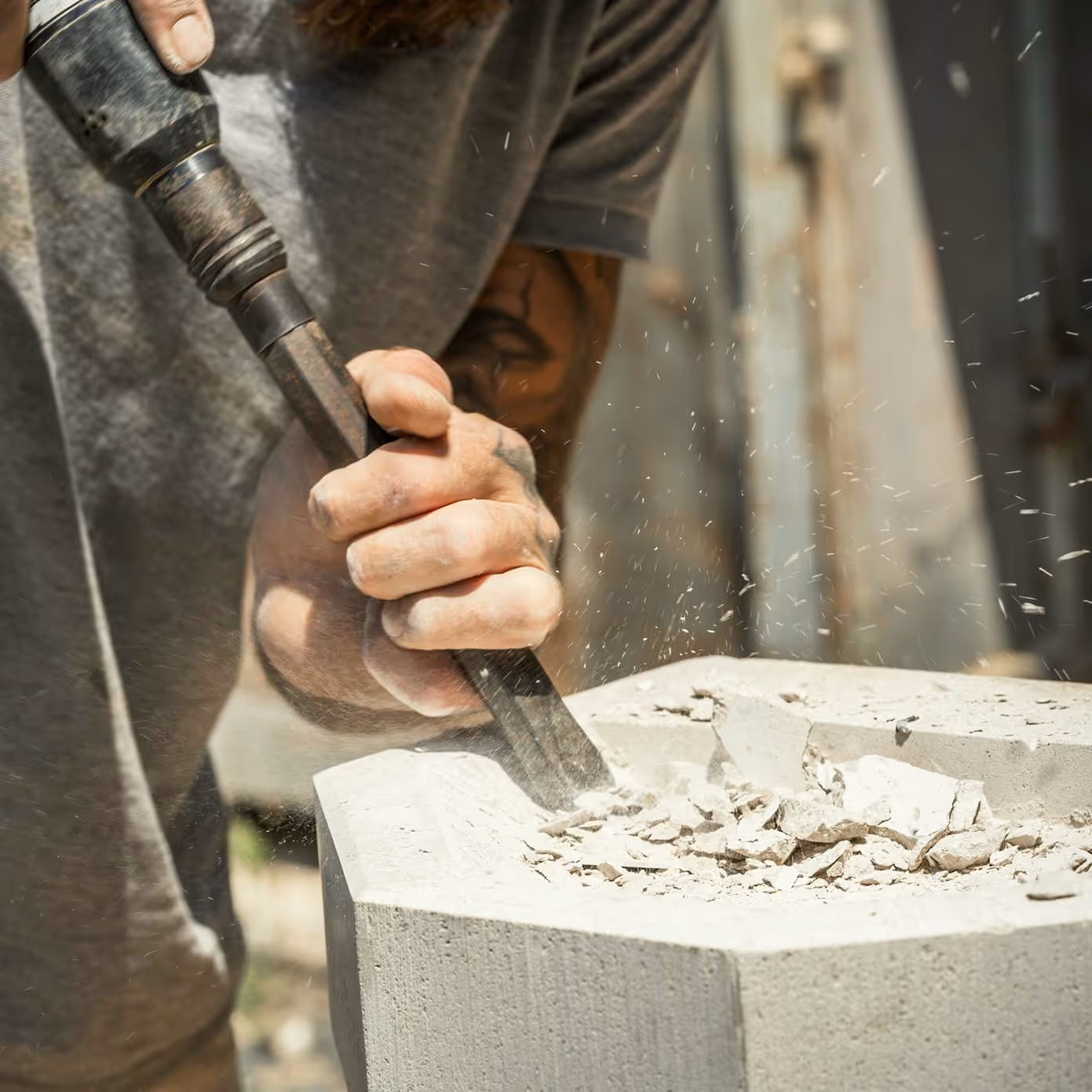 Close-up of a person chiseling a block of stone outdoors creating dust and chips.