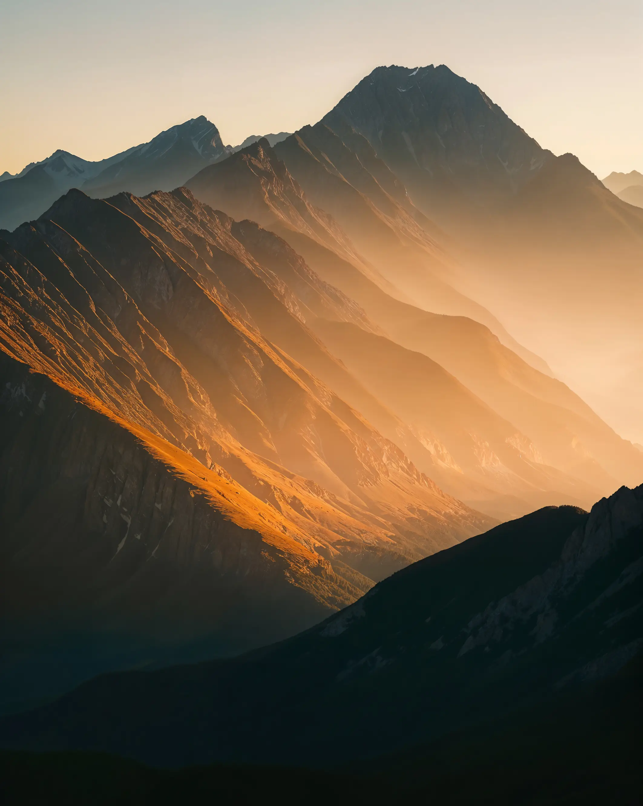 Sunlit mountain ridges with mist softly filling the valleys during sunset.