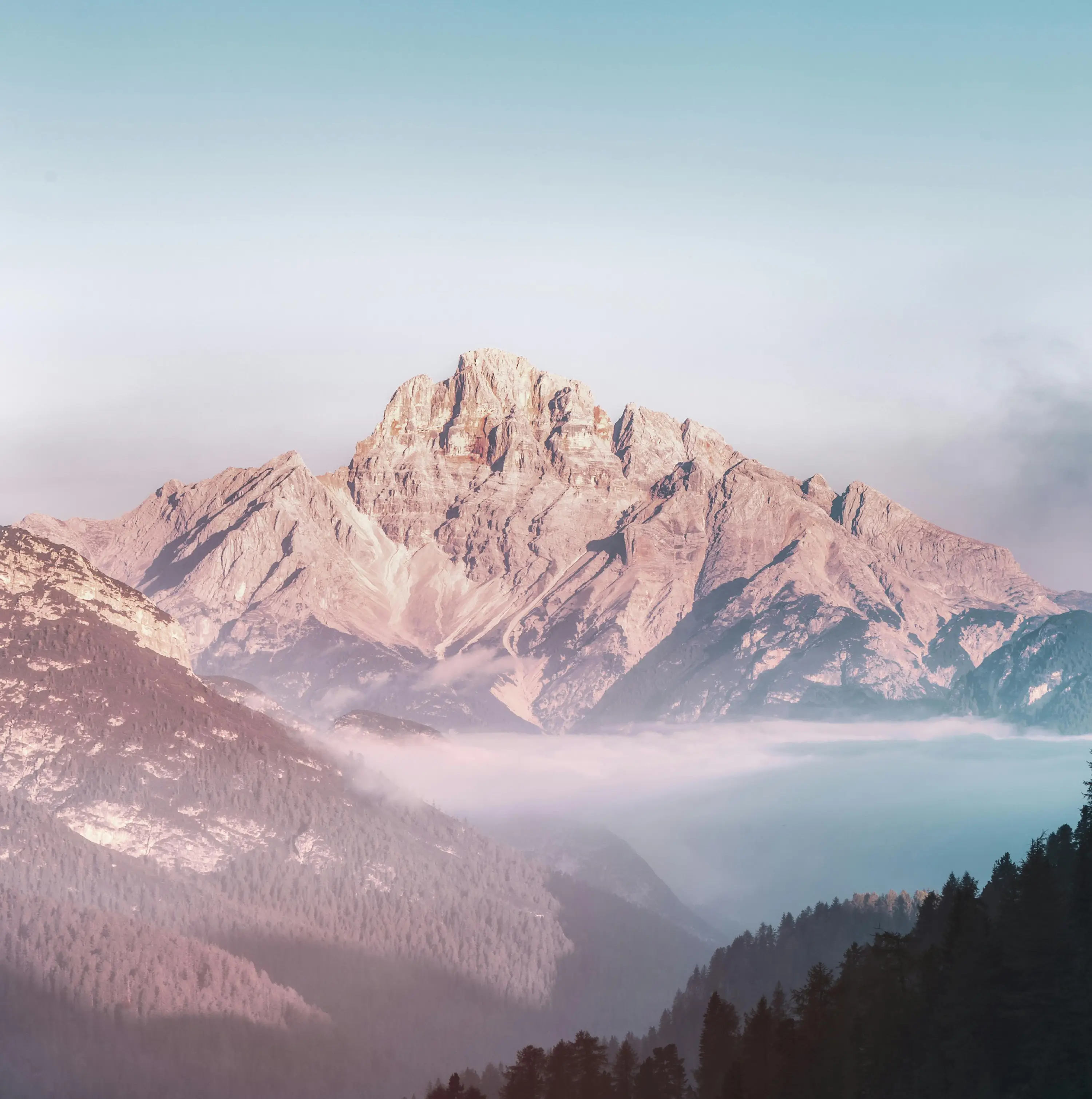 Sunlit rocky mountain peaks above a forested valley with fog rolling through.