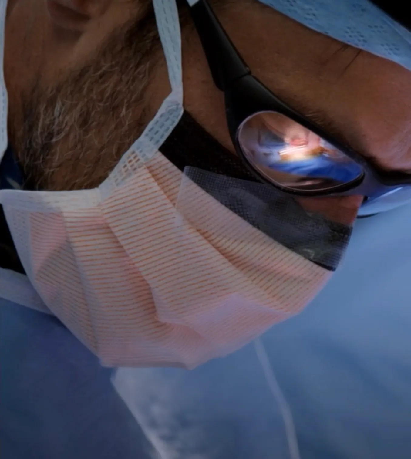 Chris Mitchell wearing surgical mask and protective glasses with operation room reflected in the lens.