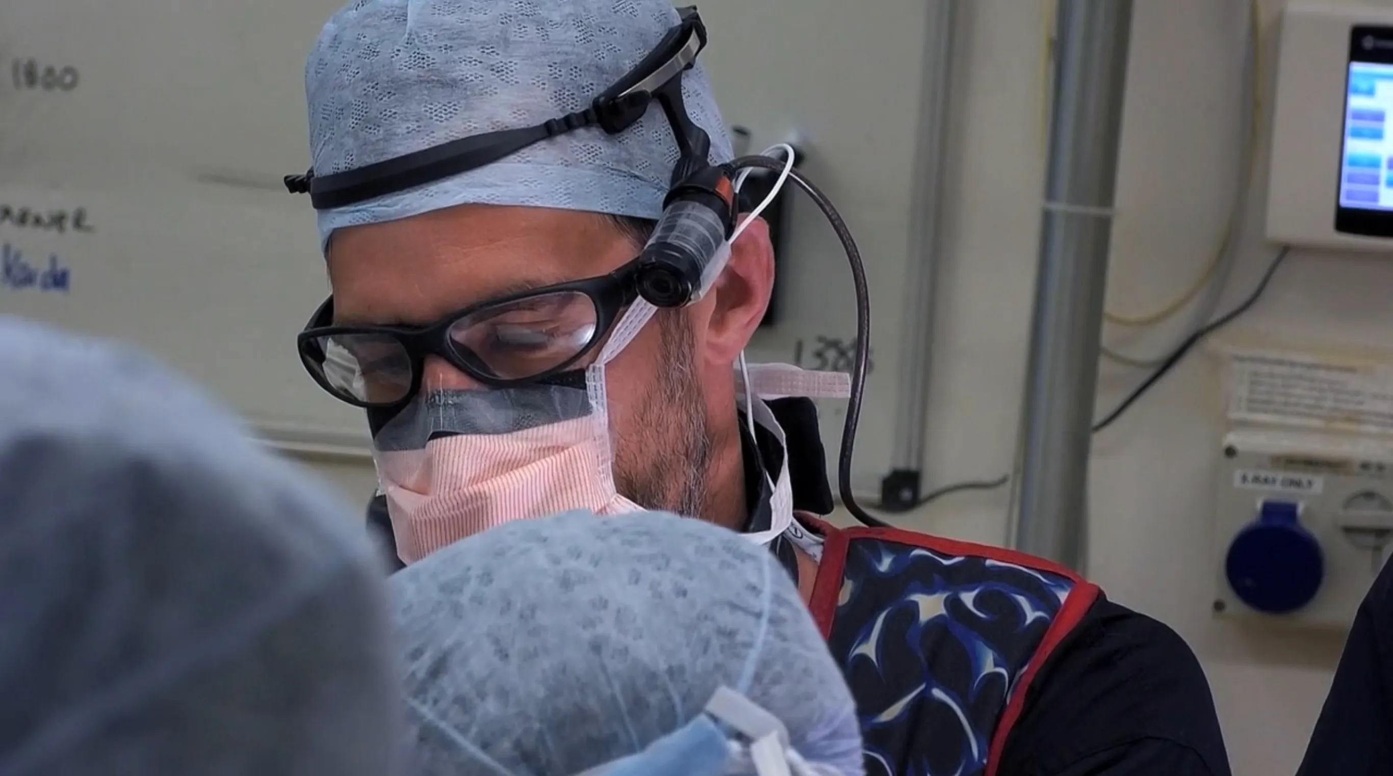 Chris Mitchell wearing surgical cap, mask, protective glasses, and headlight during a procedure.