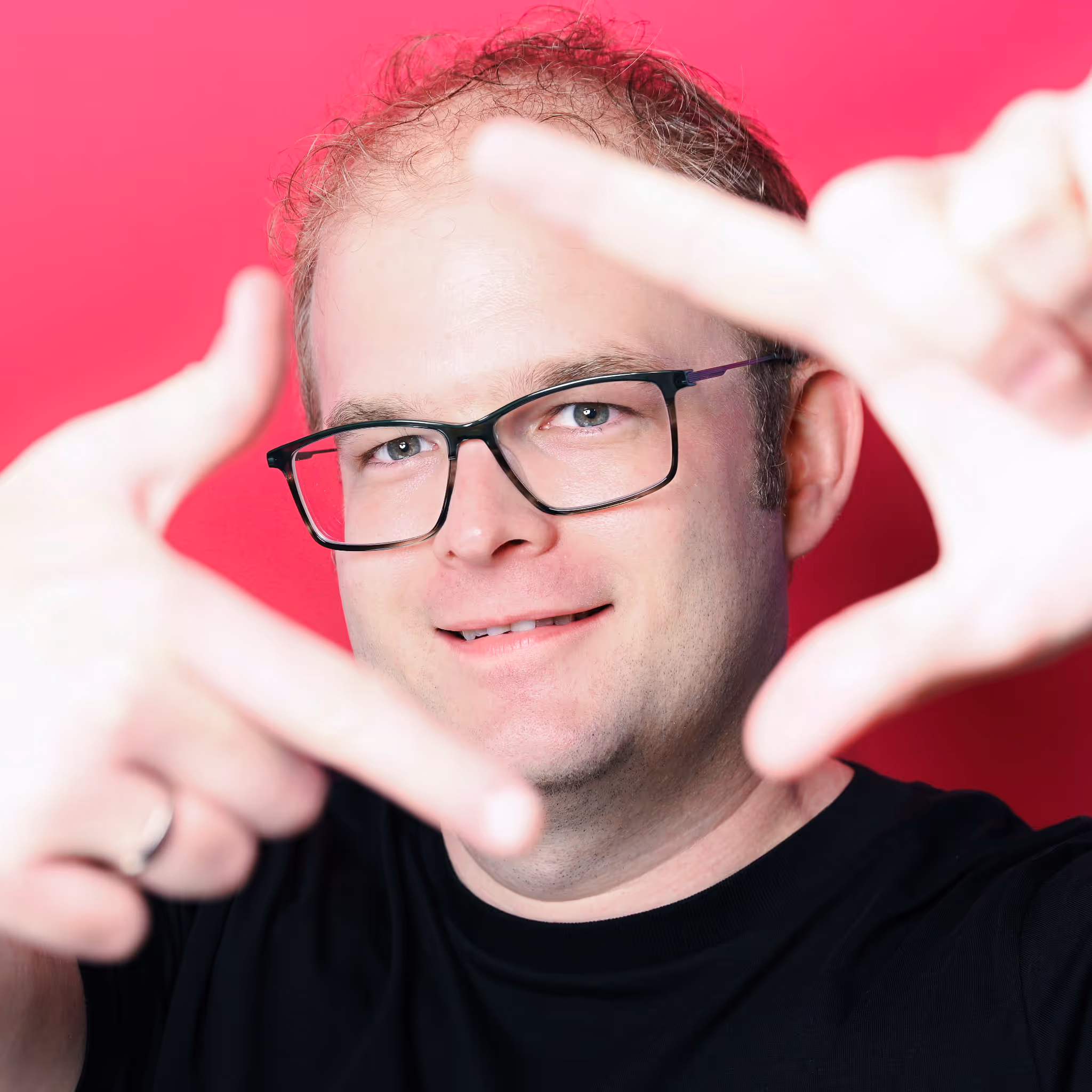 Nicolai Krämer in schwarzem Shirt vor pinkem Hintergrund, der mit den Fingern einen Rahmen formt.