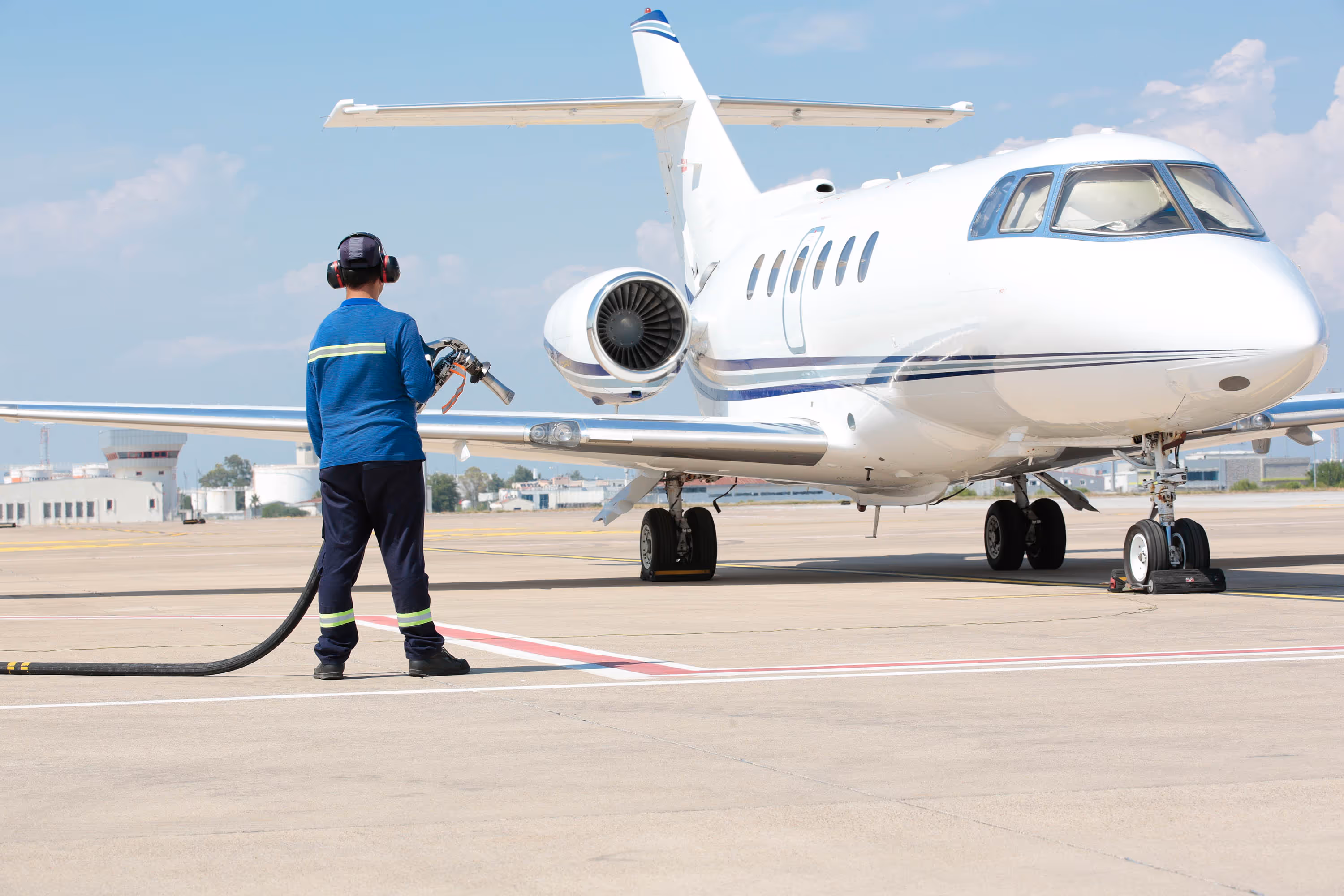 Ground crew member refueling a white private jet on an airport tarmac under a clear sky.