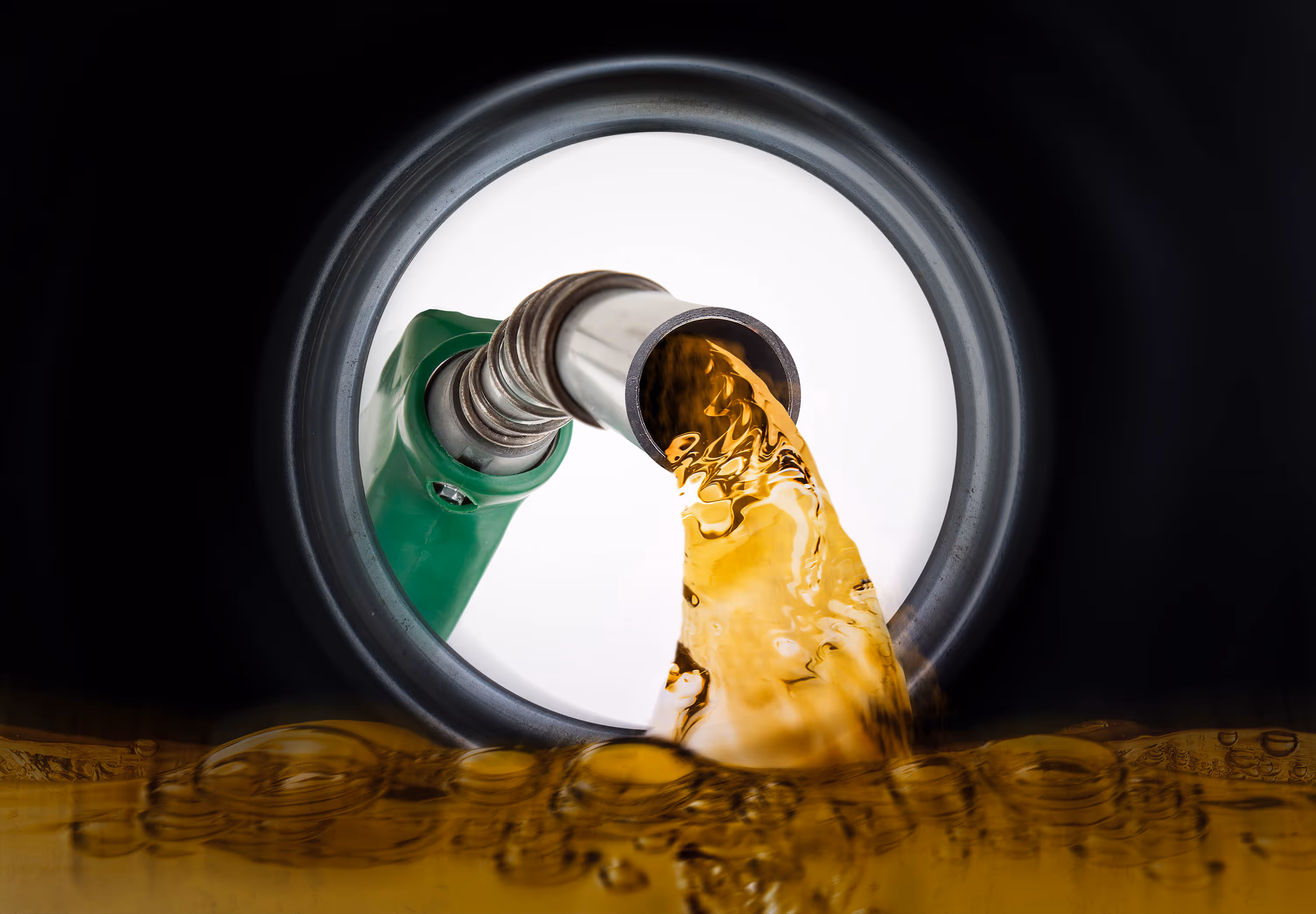 Close-up view of yellow gasoline flowing from a green fuel nozzle into a dark container.